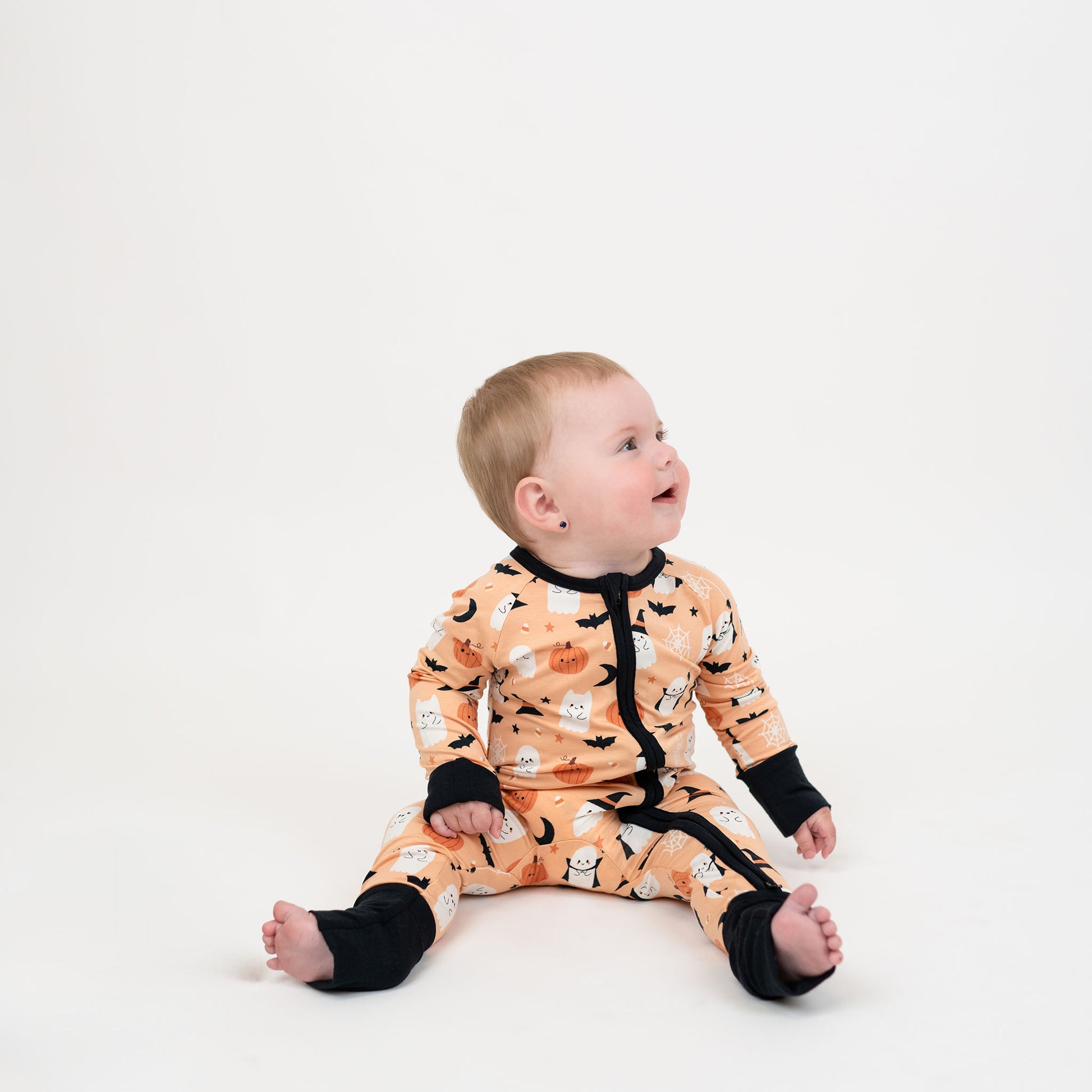 Baby wearing Boo-Tastic Halloween bamboo convertible pajamas with double zipper, featuring glow-in-the-dark ghost, pumpkin, bat, and witch hat print.