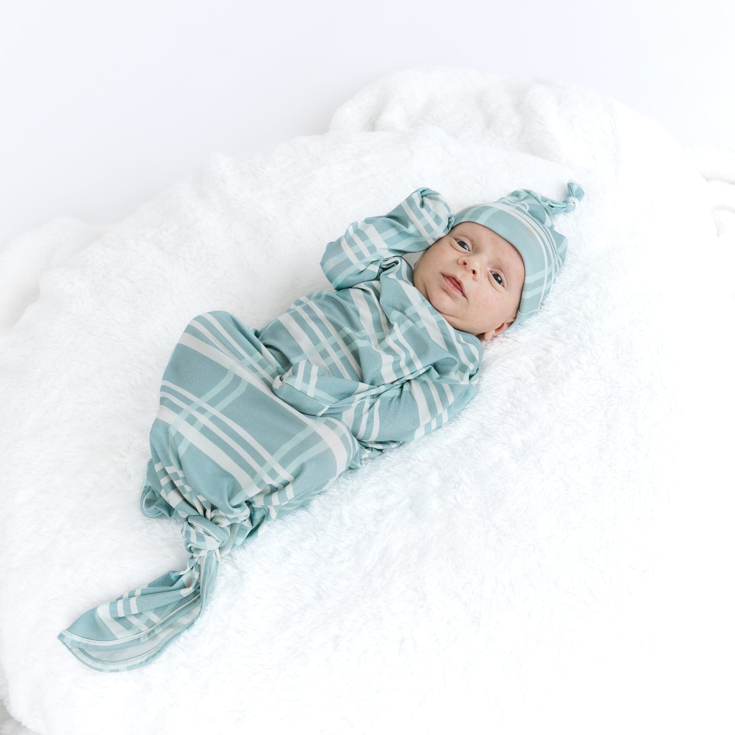 Baby wrapped in a blue and white striped swaddle with matching hat on a white background