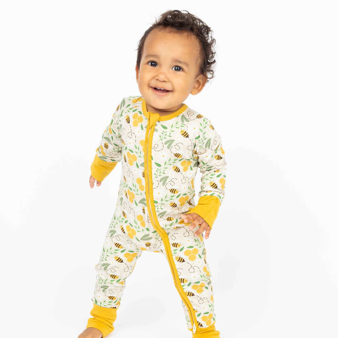 A baby standing and smiling in cozy, hypoallergenic bamboo pajamas with a honeycomb and bee print.