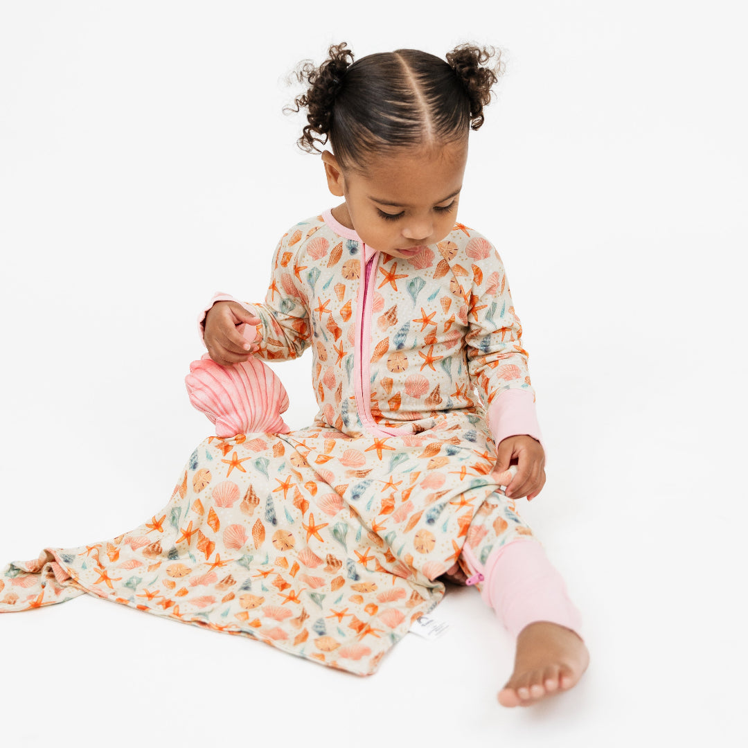 Baby lovey with sandy seashell print and pink shell with velcro with toddler in sandy seashell convertible bamboo pajamas