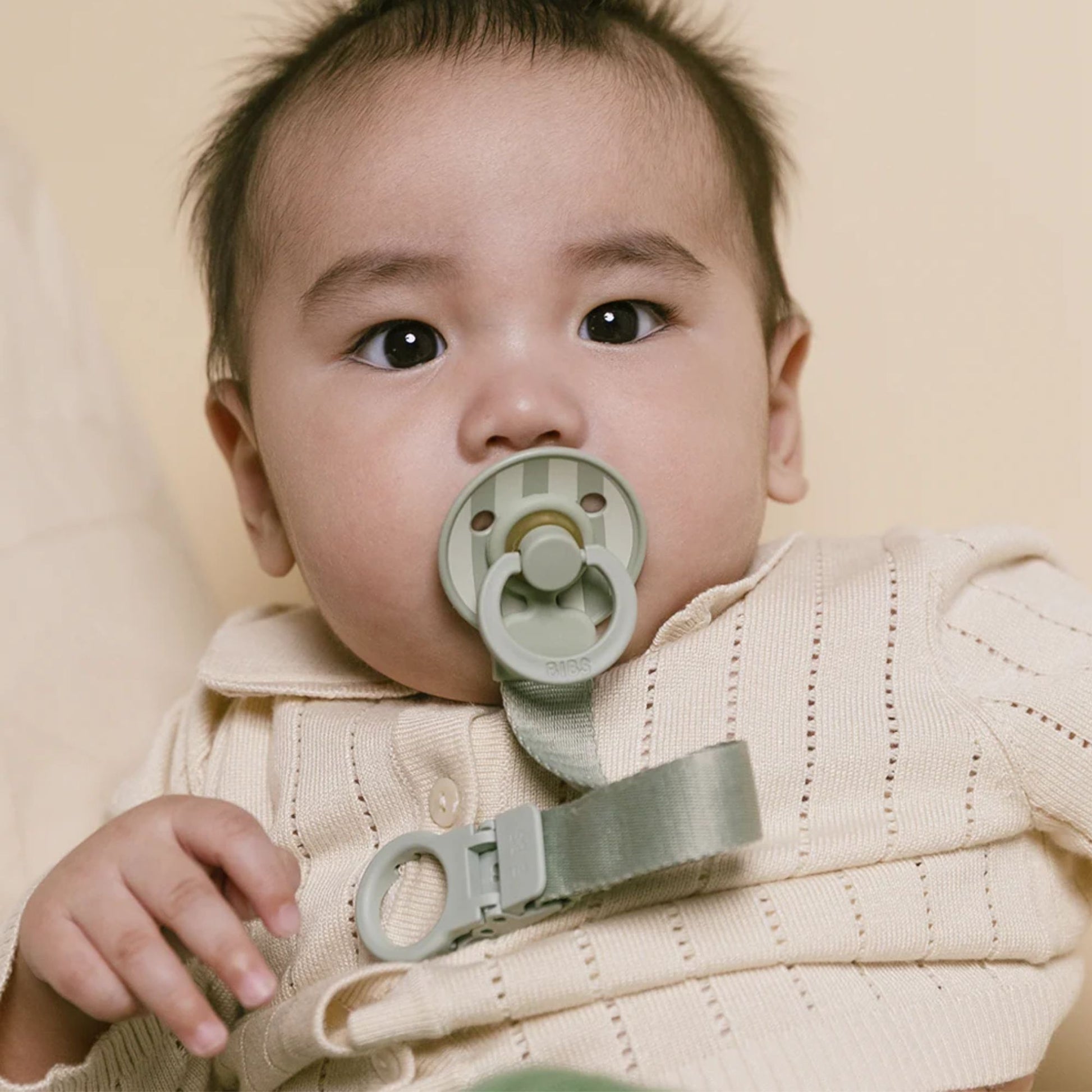 Baby wearing a beige sweater with a green pacifier