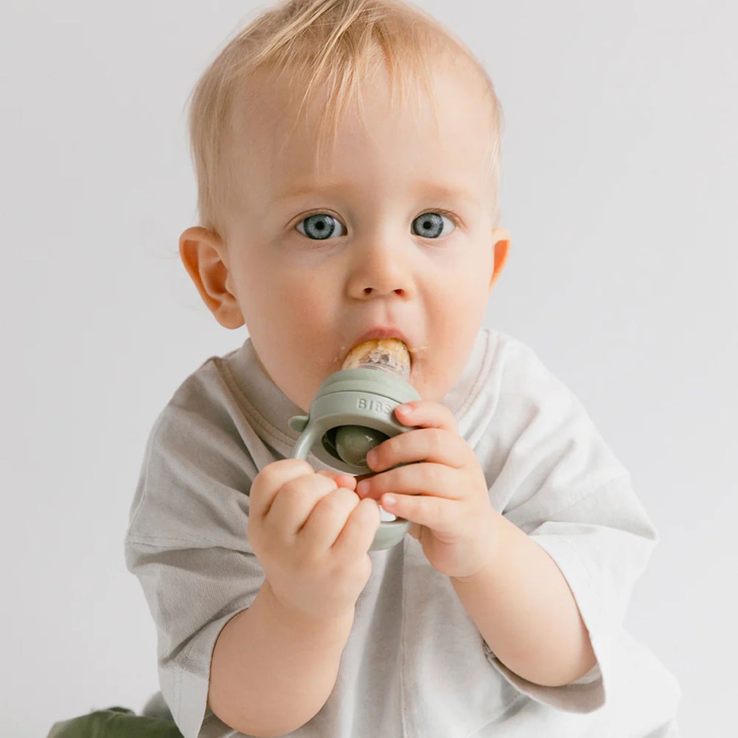 Baby holding a green teething ring against a plain background