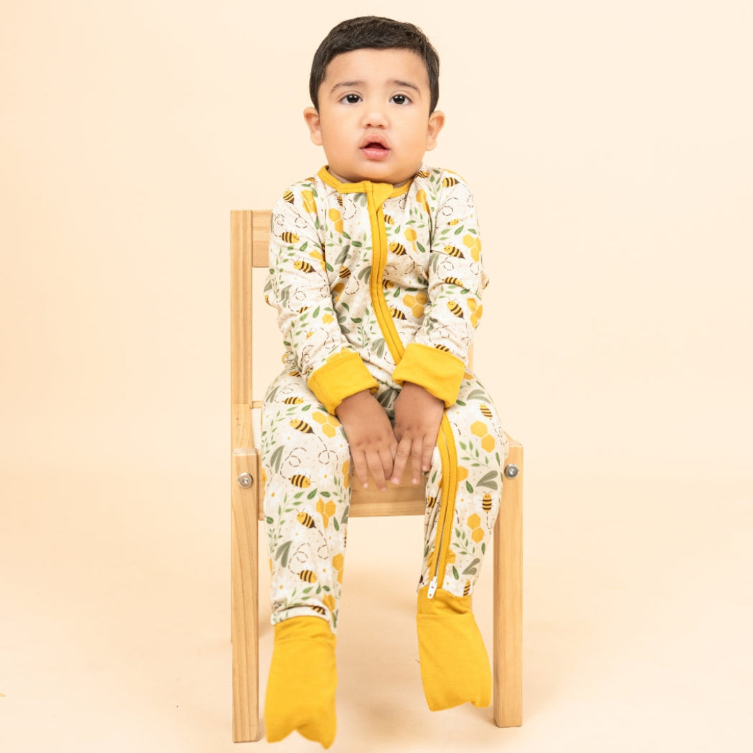 A toddler in soft, breathable, hypoallergenic bamboo pajamas with a bee print, sitting on a wooden chair.