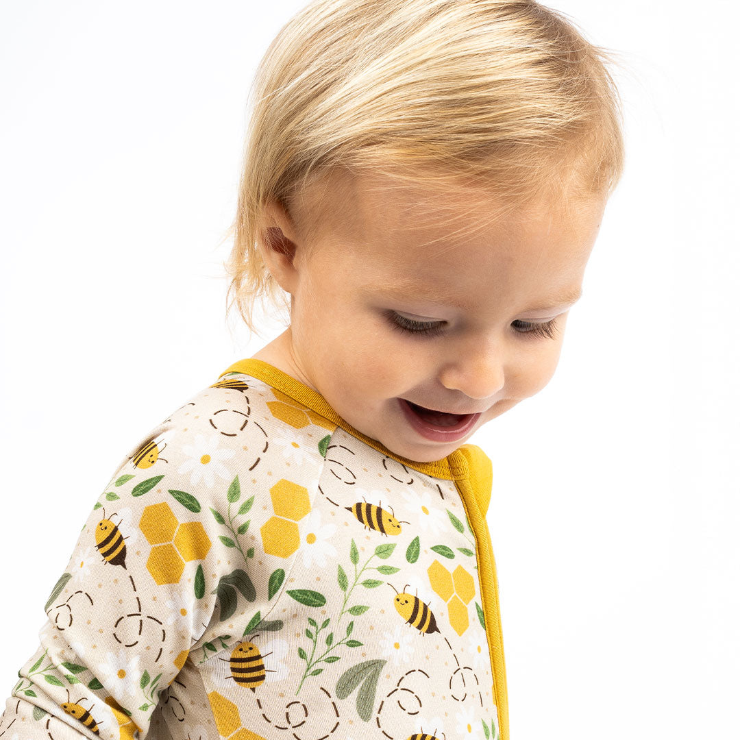 A happy blonde baby wearing breathable, hypoallergenic bamboo pajamas with a bee print, smiling with a joyful expression.