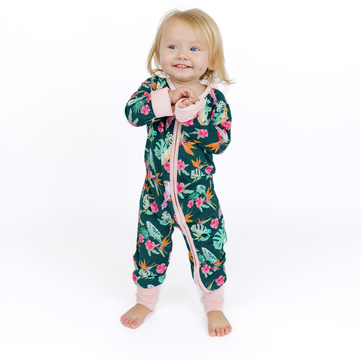 Baby standing while wearing the Isla Botánica tropical birds print bamboo romper, showing the comfortable and stretchy fit.