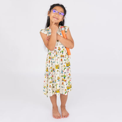 Girl wearing our twirl bamboo dress featuring playful illustrations of Arthur™ PBS Character, books, and school bus, a beige background.