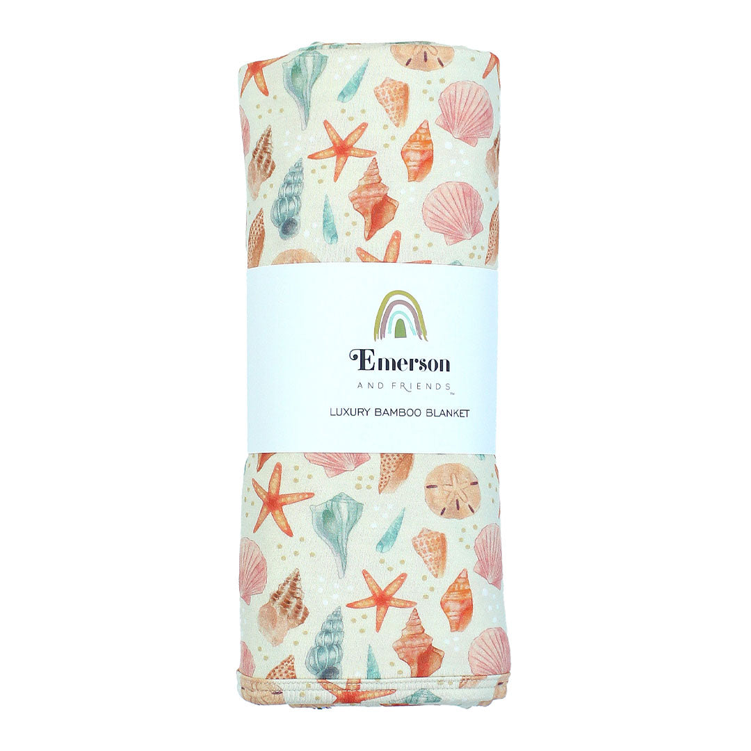 Our luxury bamboo blanket in a sandy seashell print, rolled with a label. Twin Size.