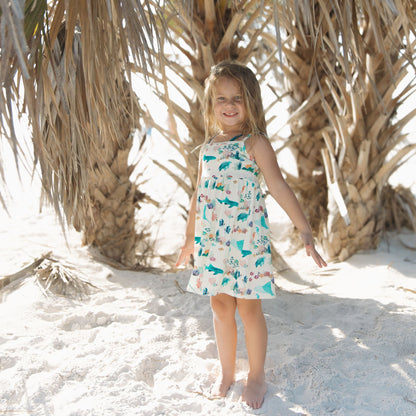 Toddler girl smiling and posing at the beach in Emerson and Friends Coral Reef Bamboo Sundress, featuring a soft, breathable fabric with an ocean-themed print of sharks, sea turtles, and coral, designed for lightweight summer comfort and easy movement.