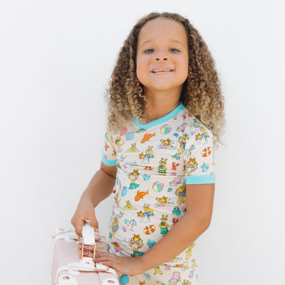 Toddler girl wearing our Arthur's Family Vacation Bamboo Short Sleeve Kids Pajama Pants Set featuring vibrant light blue trim and a playful print of Arthur™ in swimwear surrounded by fun beach props — perfect for family getaways.