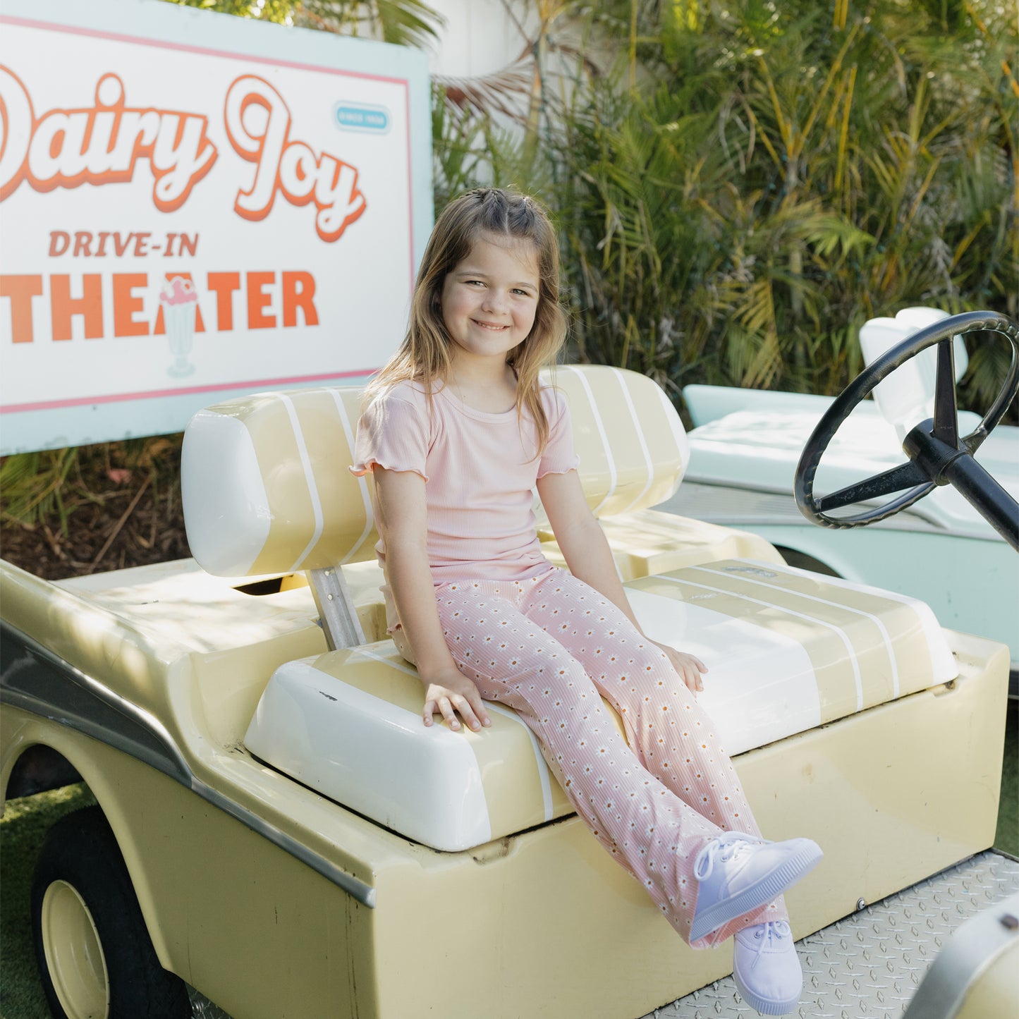 Young girl sitting in a miniature car with a Dairy Joy Drive-In Theater sign in the background