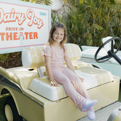 Young girl sitting in a miniature car with a Dairy Joy Drive-In Theater sign in the background