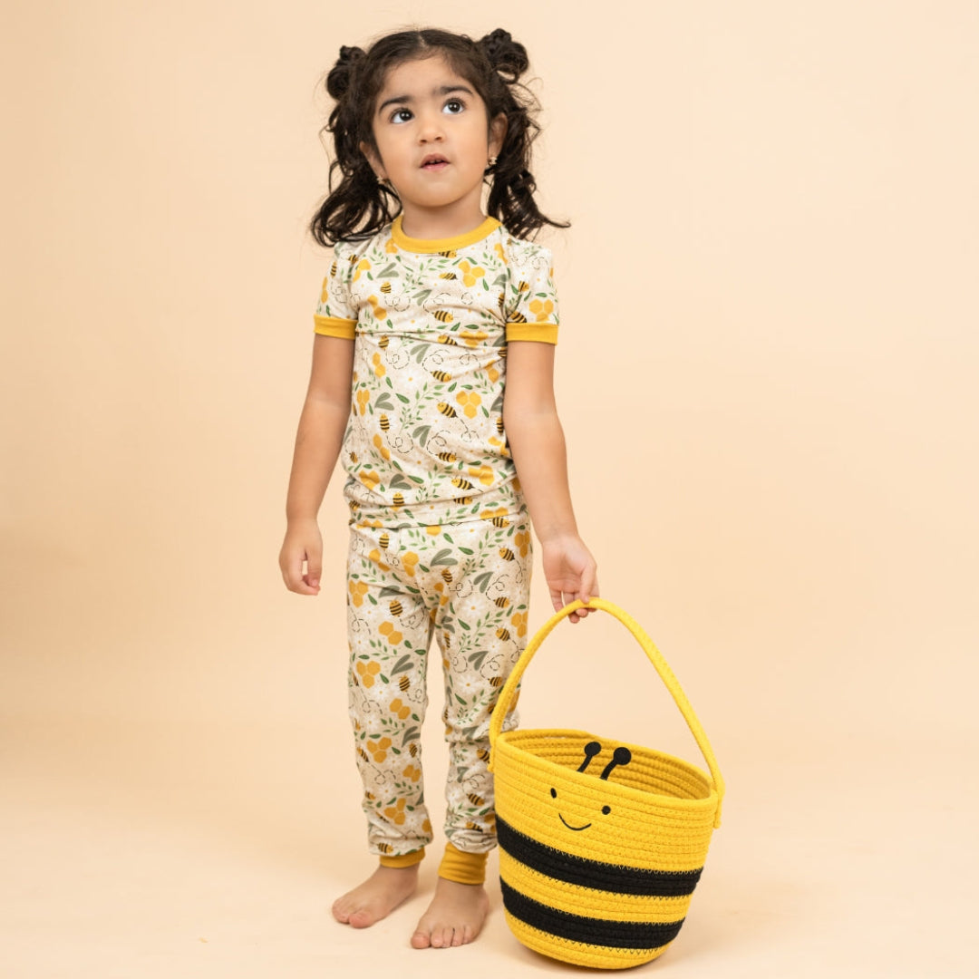 A young girl wearing soft bamboo kids' pajamas with a honey bee print, holding a yellow and black bee basket, perfect for springtime.