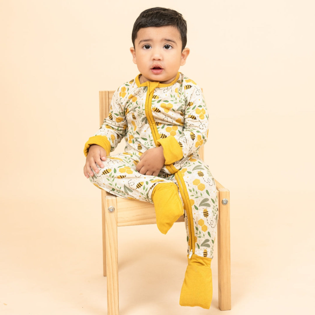 A toddler in cozy, soft bamboo pajamas with a honeycomb and bee print, sitting on a wooden chair with covered feet.