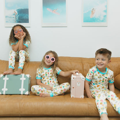 Siblings wearing our Arthur's Family Vacation Bamboo Short Sleeve Kids Pajama Pants Set featuring vibrant light blue trim and a playful print of Arthur™ in swimwear surrounded by fun beach props — perfect for family getaways.