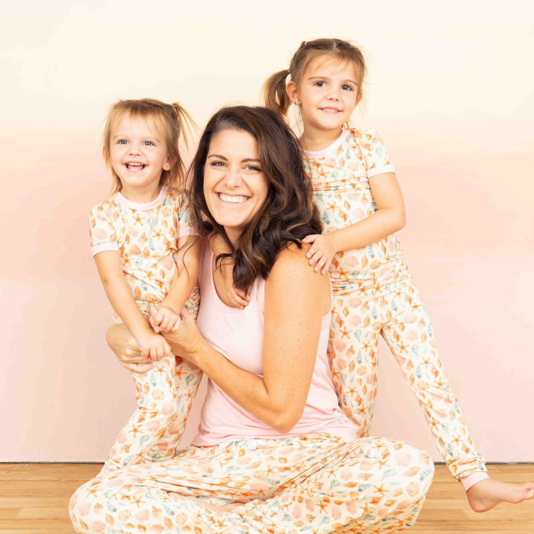 Woman with two toddler girls matching in our sandy Seashell print. She is wearing our Bubblegum pink tank top with the relaxed pants and the toddler girls are matching with our 2 piece set. 