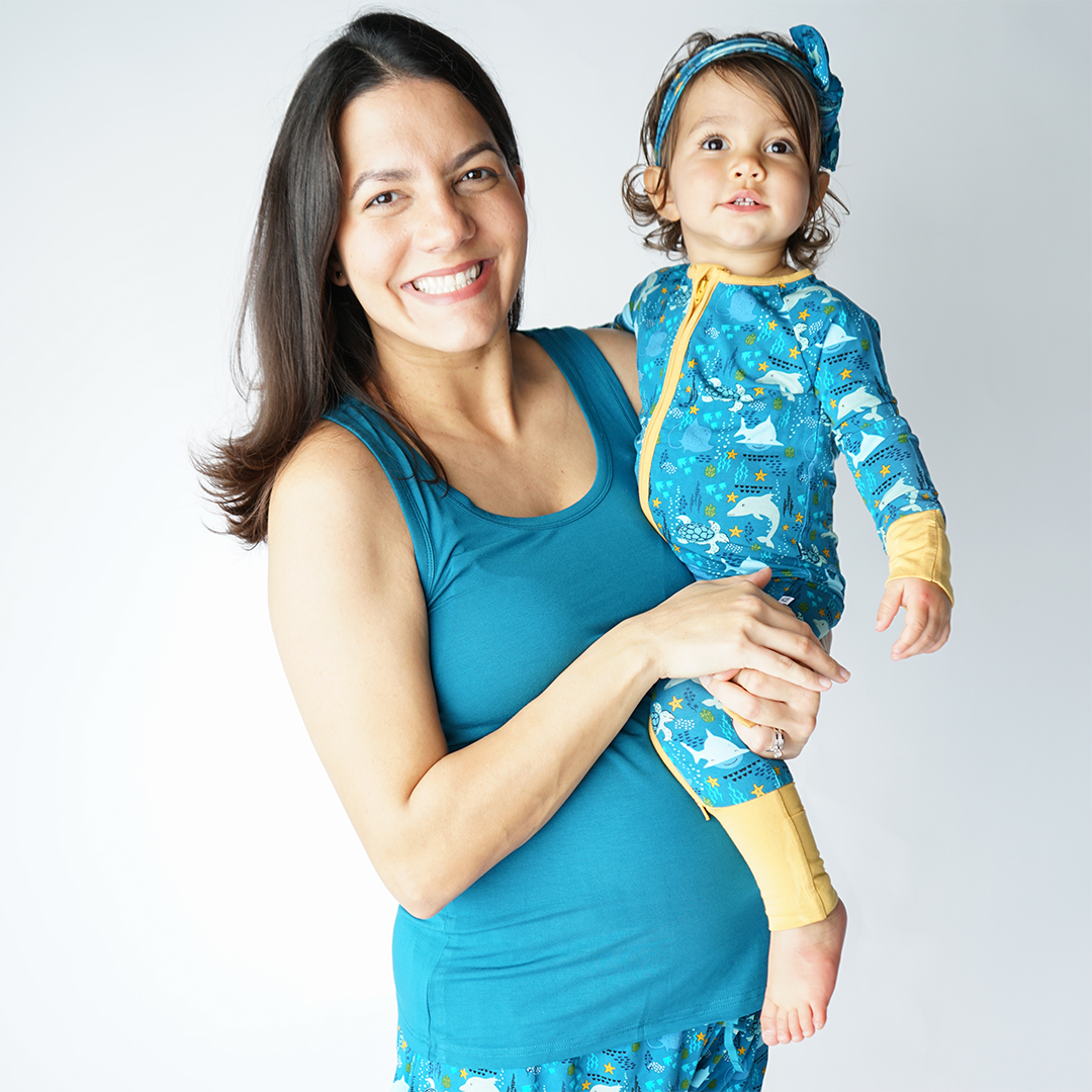 mom holds her baby on her hip. the baby is in the "ocean friends" convertible and baby headband. the mom wears the ocean blue women's tank top. 