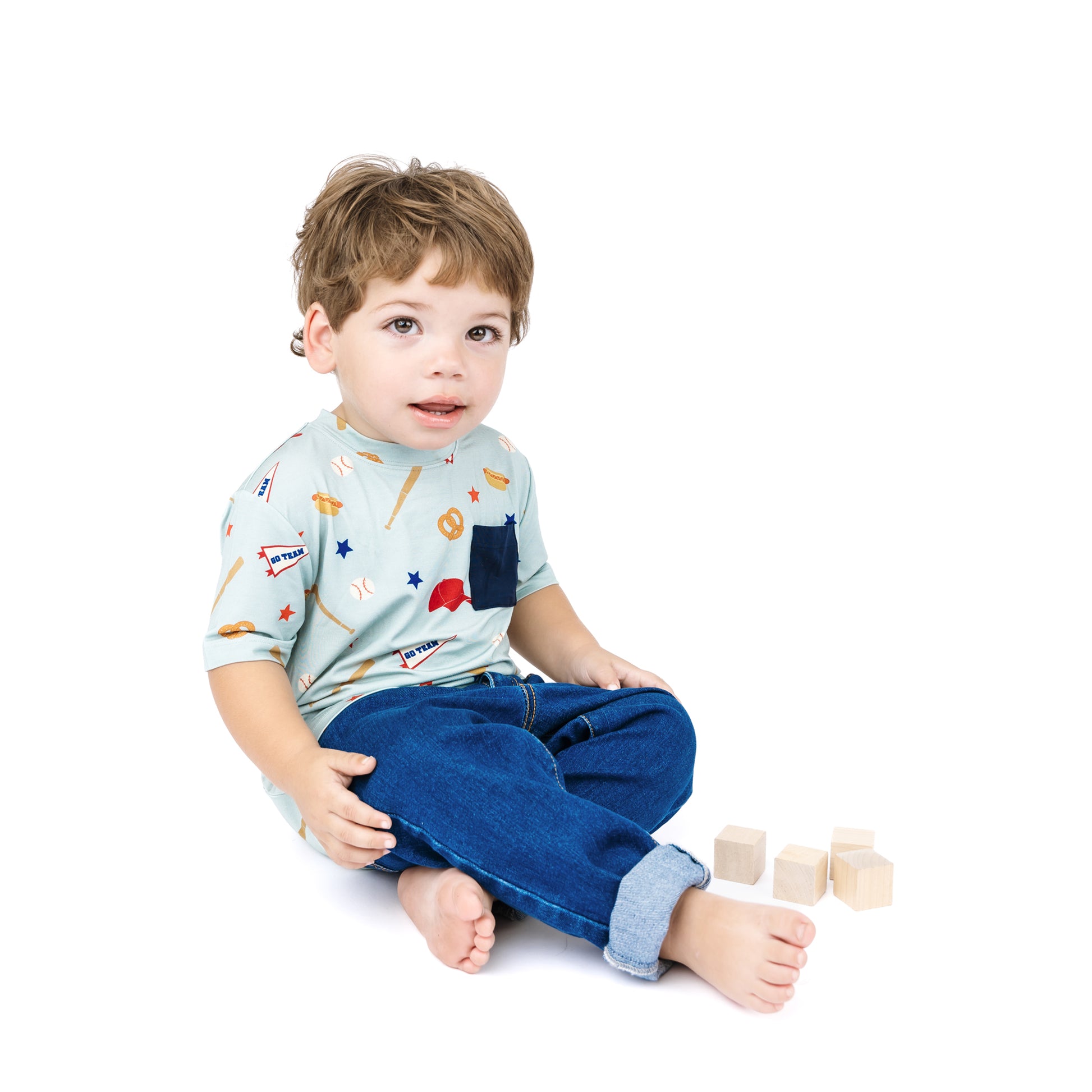 Child wearing a light blue shirt with colorful patterns and dark blue jeans, sitting on a white background.