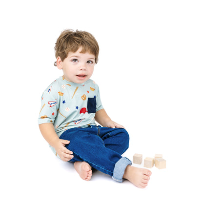 Child wearing a light blue shirt with colorful patterns and dark blue jeans, sitting on a white background.