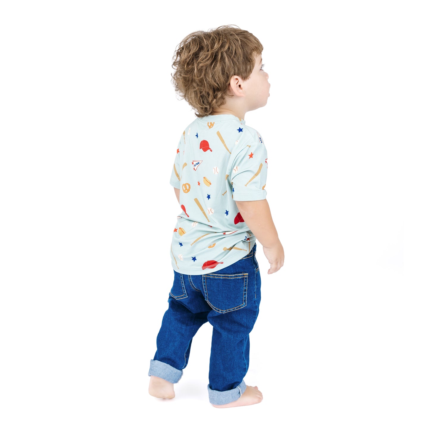 Child wearing a light blue shirt with colorful patterns and blue jeans on a white background