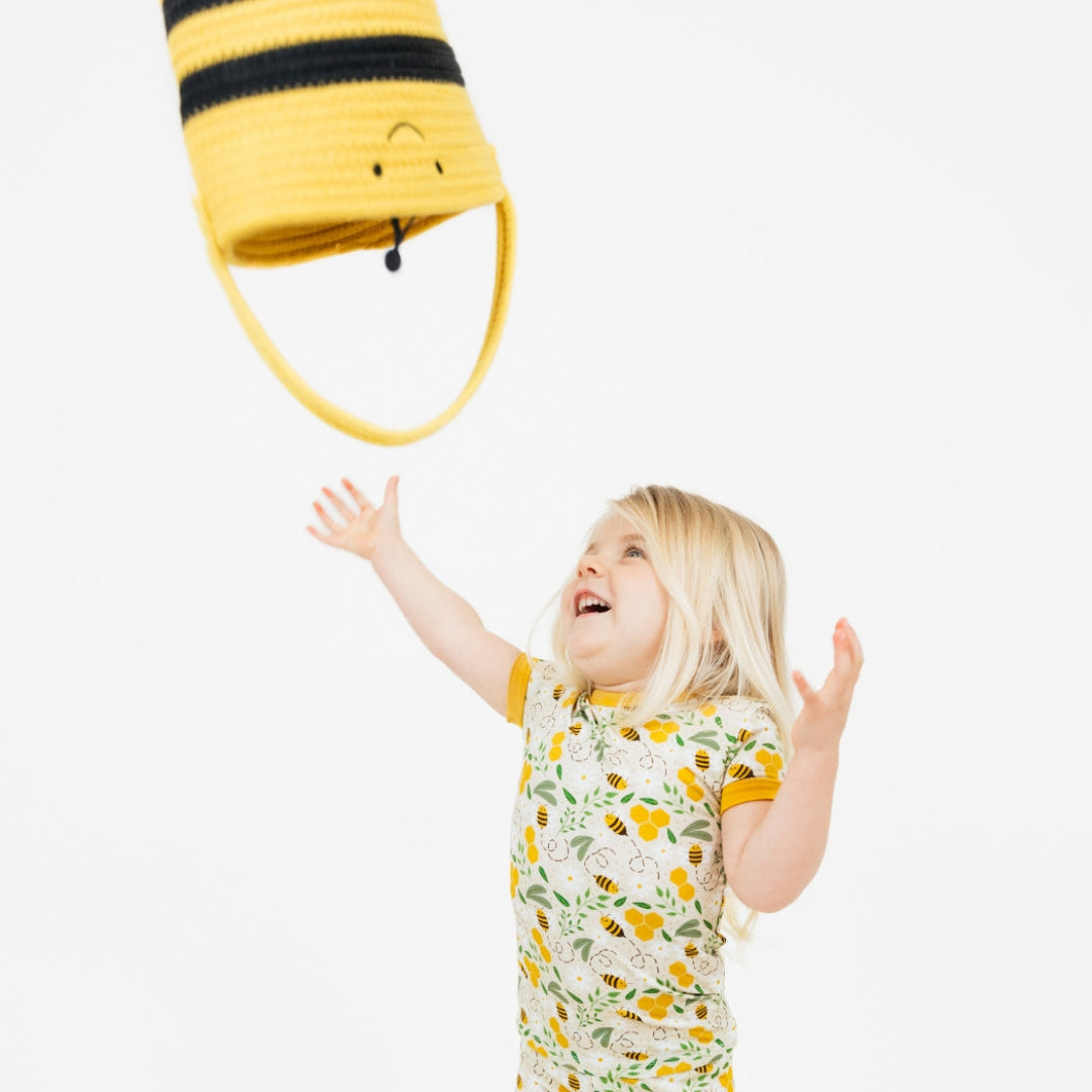 A joyful child tossing a yellow and black bee-themed rope basket in the air, ideal for playroom storage and Easter egg hunts