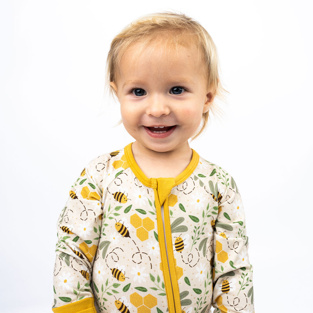 A baby happily wearing breathable bamboo pajamas with a bee print, featuring a convertible design for extra comfort.