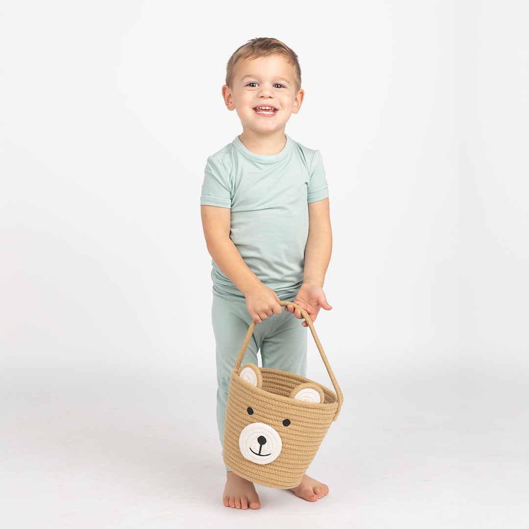 young boy stands and smiles with his bear rope basket. 