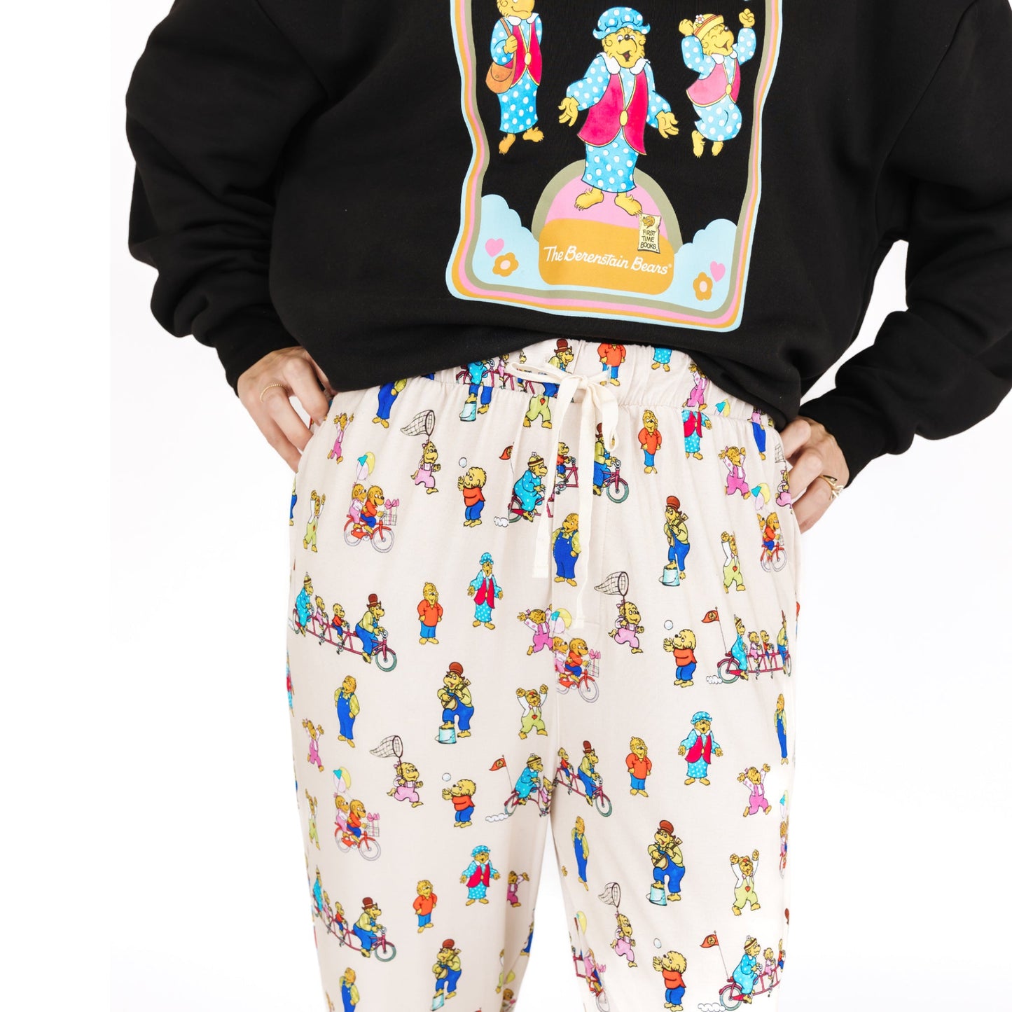 Person wearing a black hoodie with a colorful graphic and white pants with a bear pattern on a white background