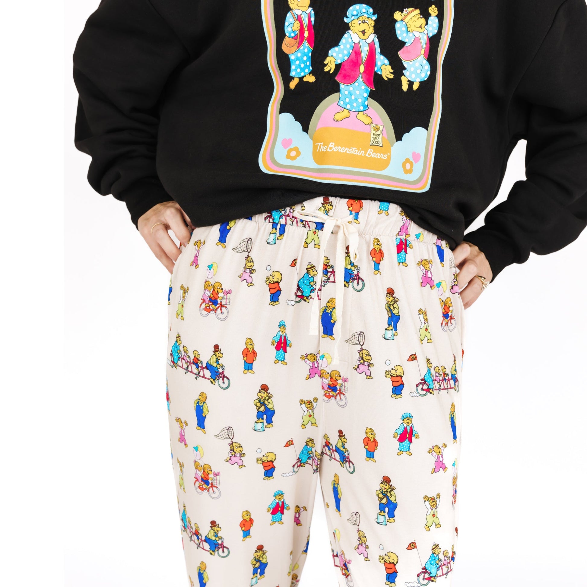 Person wearing a black hoodie with a colorful graphic and white pants with a bear pattern on a white background