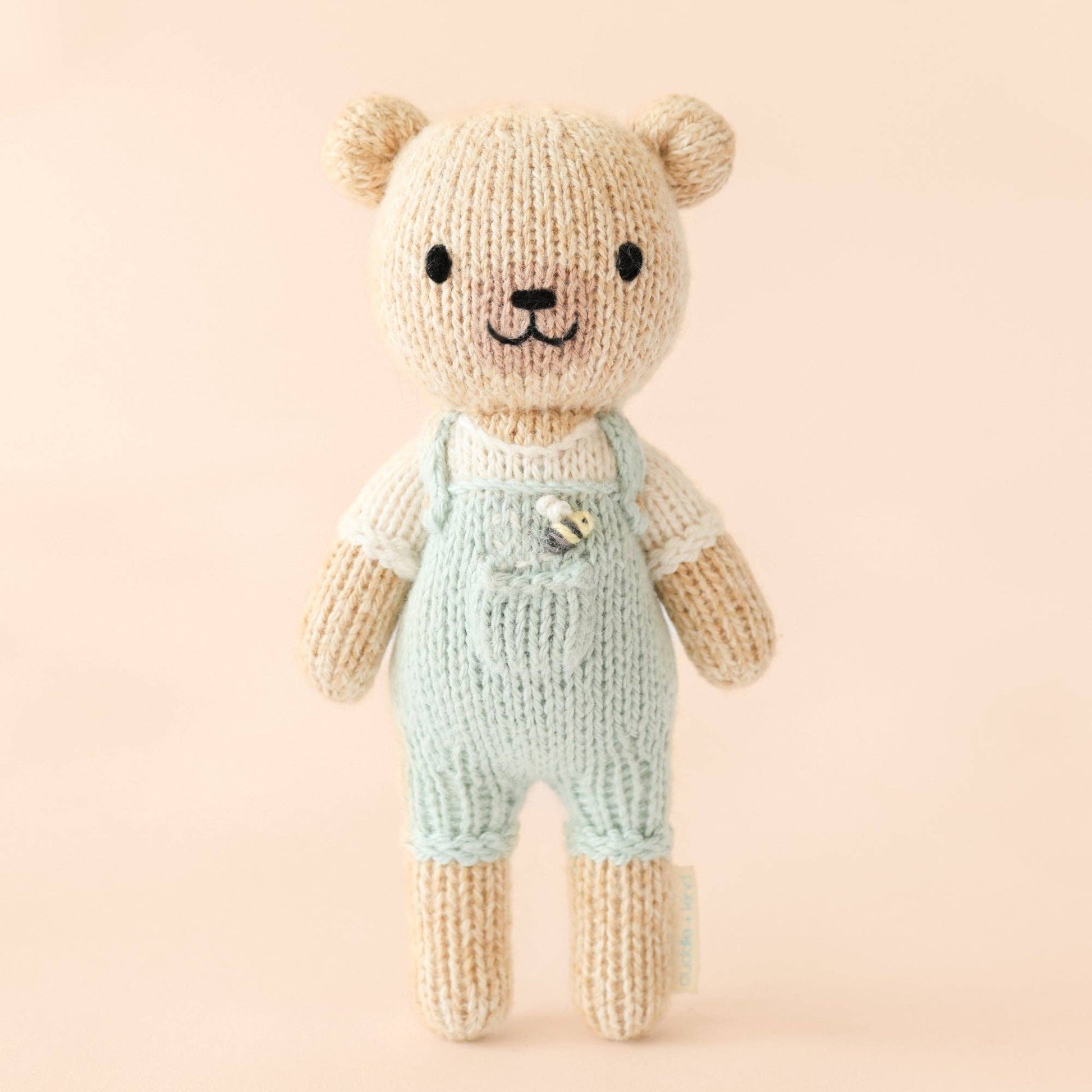 Knitted teddy bear wearing overalls on a pink background