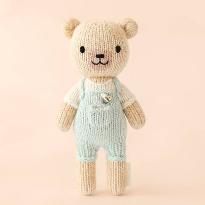 Knitted teddy bear wearing overalls on a pink background