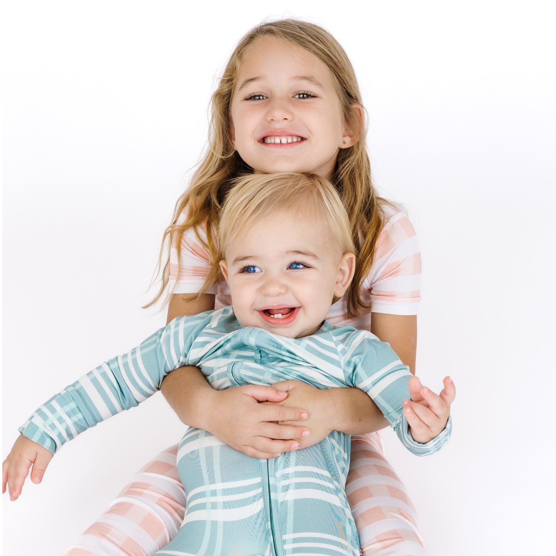 Two young children, an older girl and a younger boy, are hugging each other on a white background.