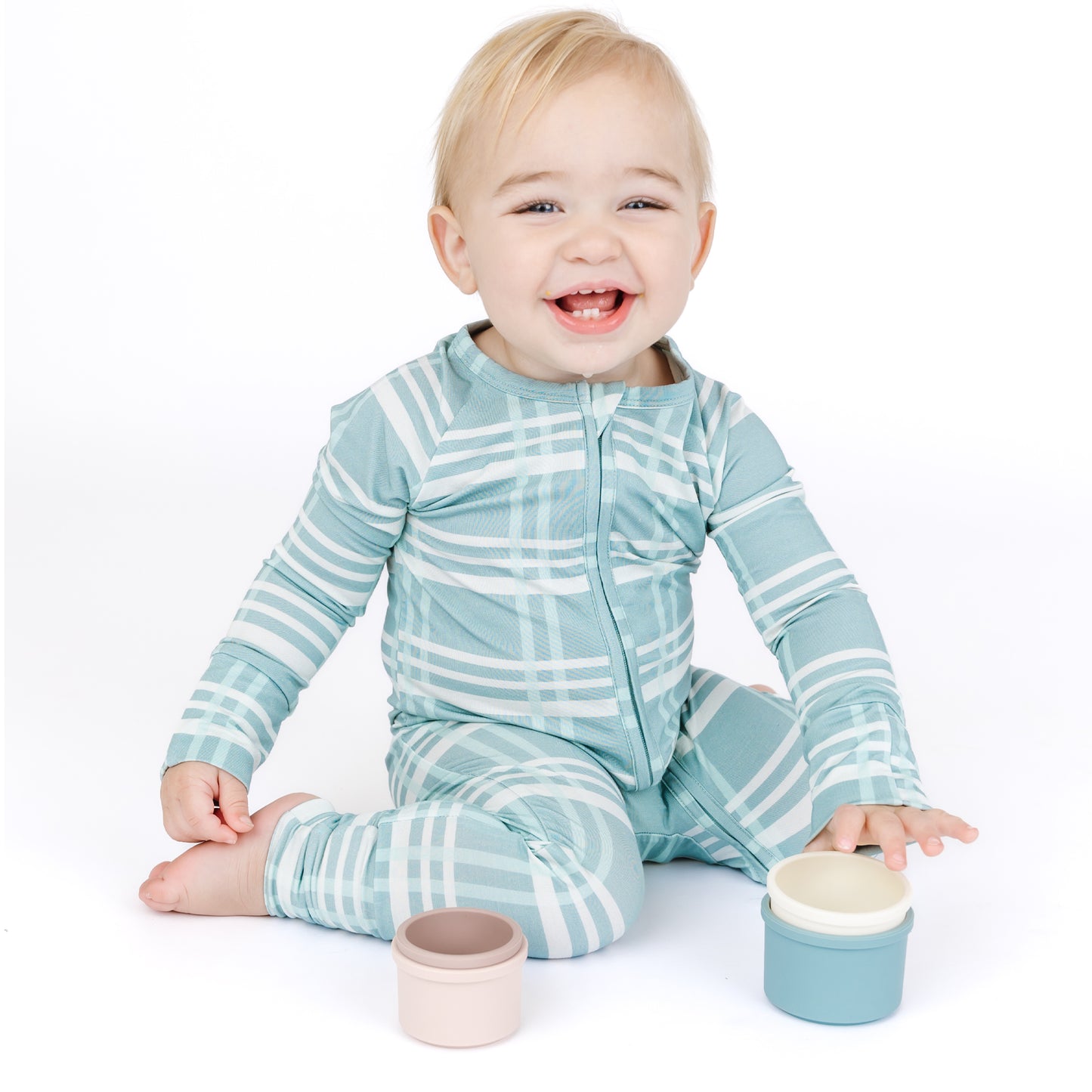 Baby wearing a blue and white striped onesie sitting on a white background with two containers.