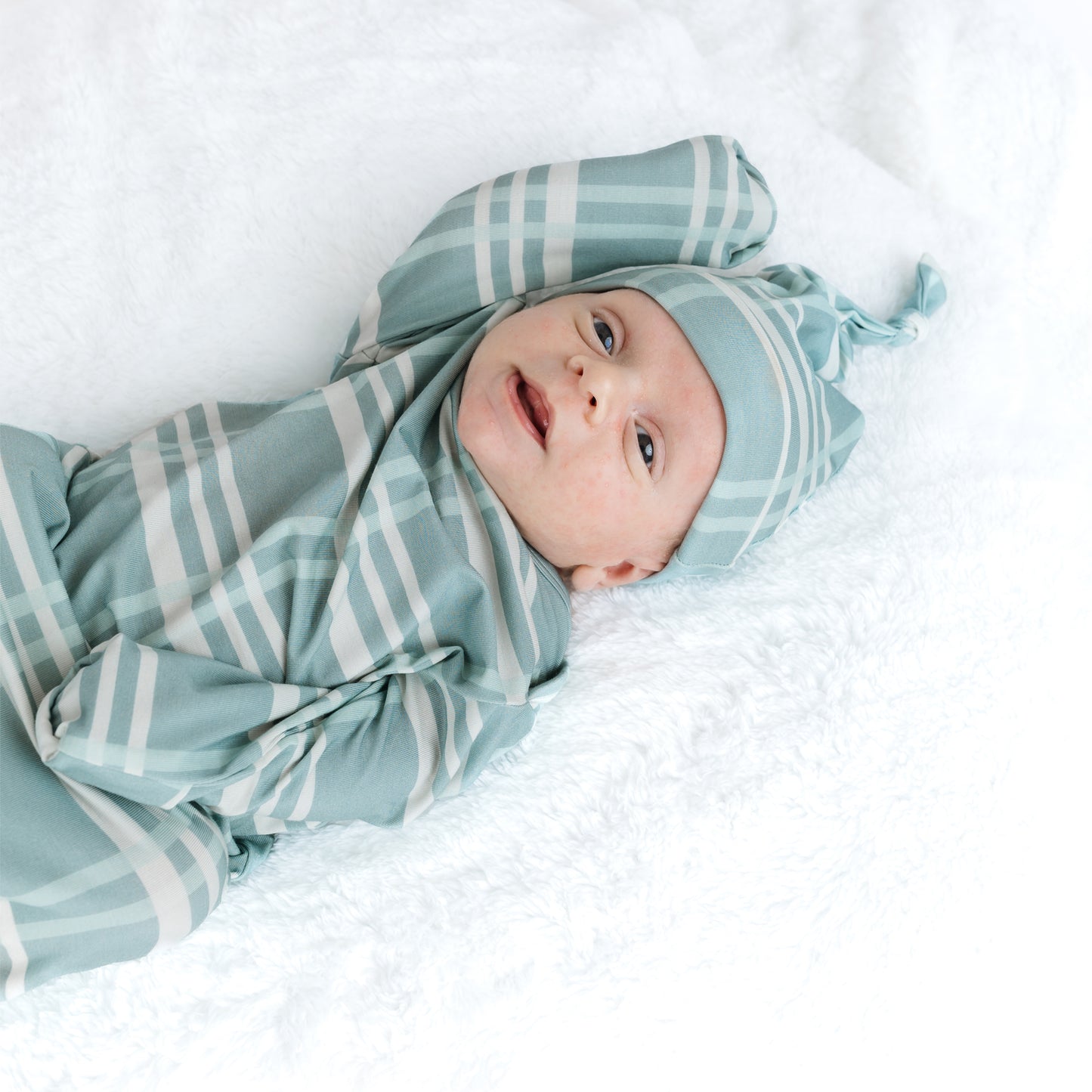 Baby wrapped in a blue and white striped swaddle with matching headband on a white background