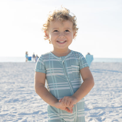 Child wearing a light blue and white checkered outfit on a sandy beach.