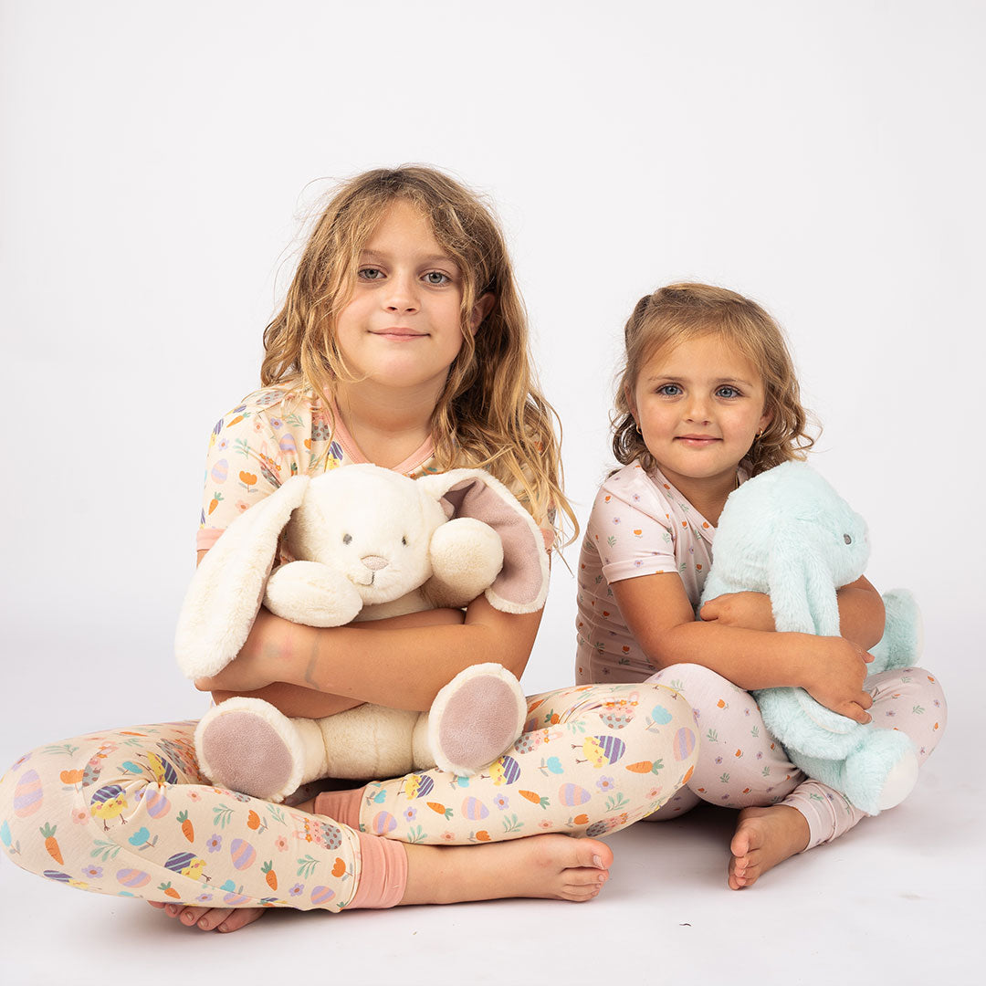 2 girls sit side by side, holding the white and blue easter bunnies in their laps. 