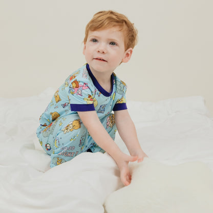 A toddler boy wearing our PBS Good Night Arthur™ collaboration, featuring pajamas adorned with Arthur and his friends in a cozy bedtime scene. The design includes storybooks, toothbrushes, bunny slippers, a sleeping puppy, crescent moons with sleep caps, twinkling stars, and the words 'GOOD NIGHT!' on a soft blue background.