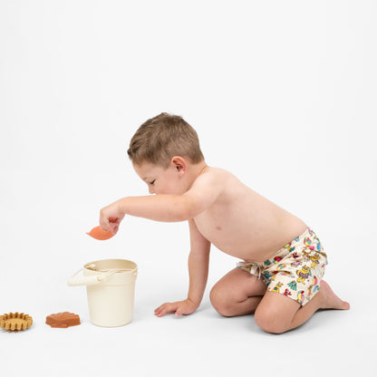 Toddler boy playing and wearing Emerson and Friends Arthur's™ Family Vacation Boys Swim Trunks, featuring a fun beach-themed print with Arthur and friends, adjustable drawstring waist, and quick-dry fabric for a comfortable and stylish swimwear option.