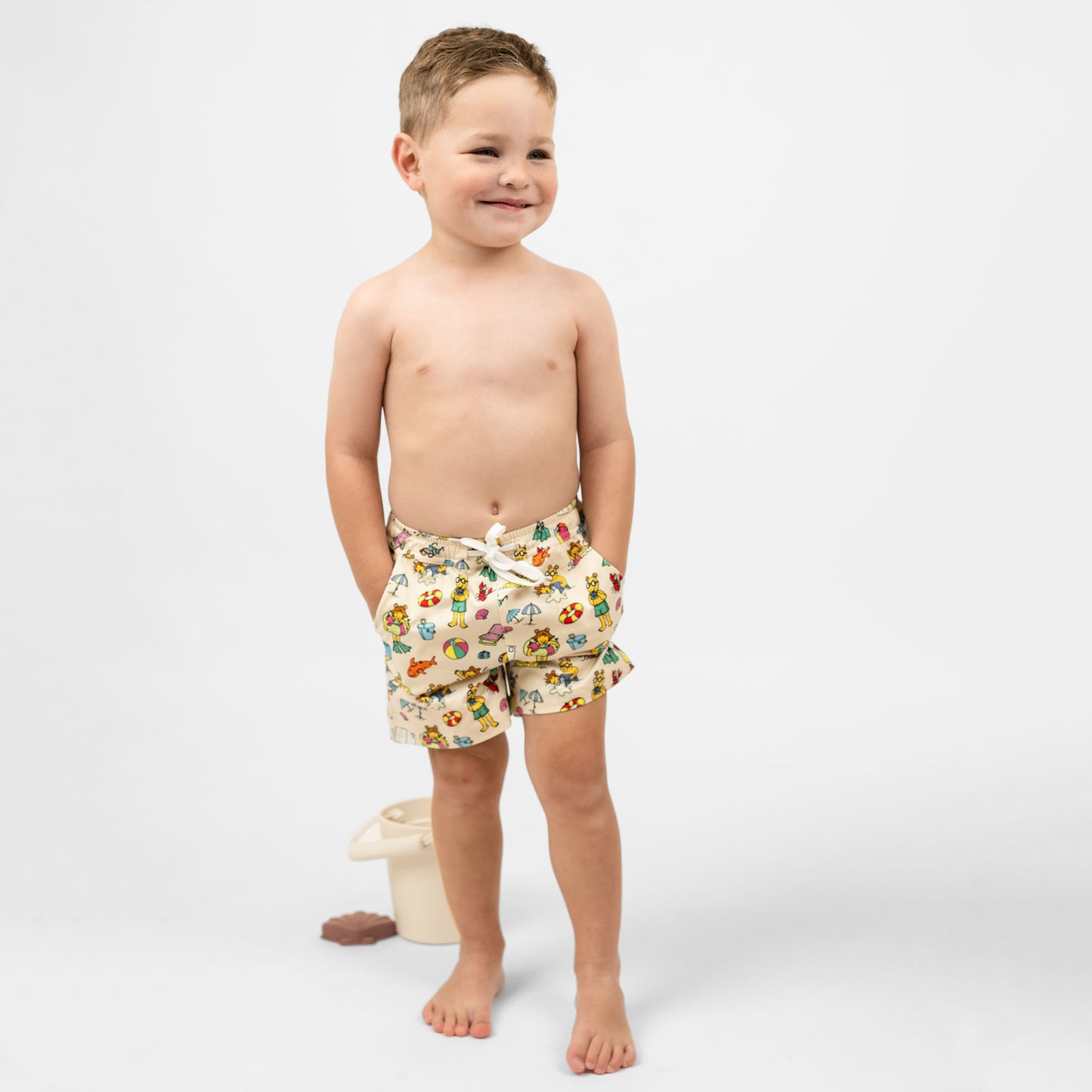 Toddler boy wearing Emerson and Friends Arthur's™ Family Vacation Boys Swim Trunks, featuring a fun beach-themed print with Arthur and friends, adjustable drawstring waist, and quick-dry fabric for a comfortable and stylish swimwear option.