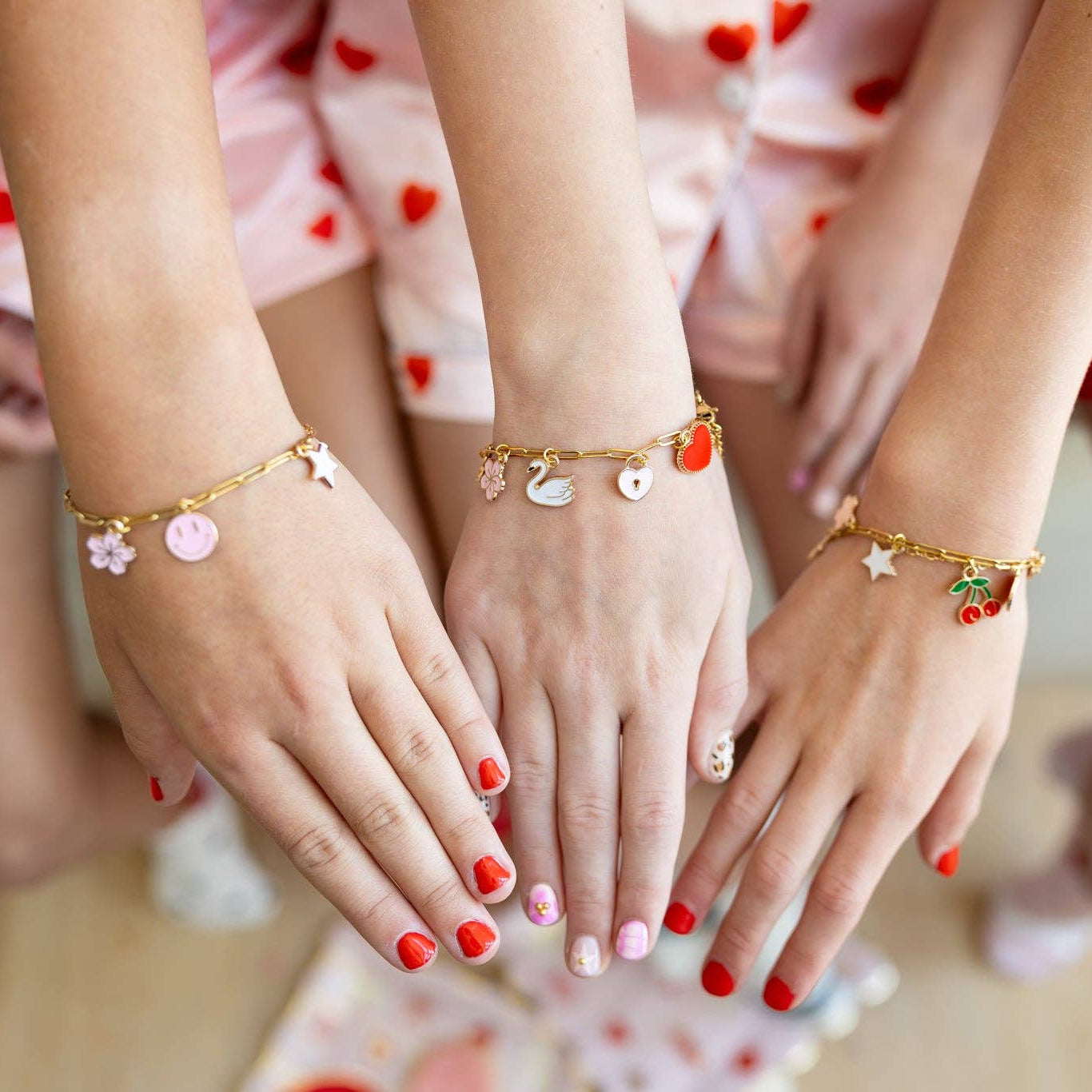 Three hands wearing gold bracelets with various charms on a blurred background.