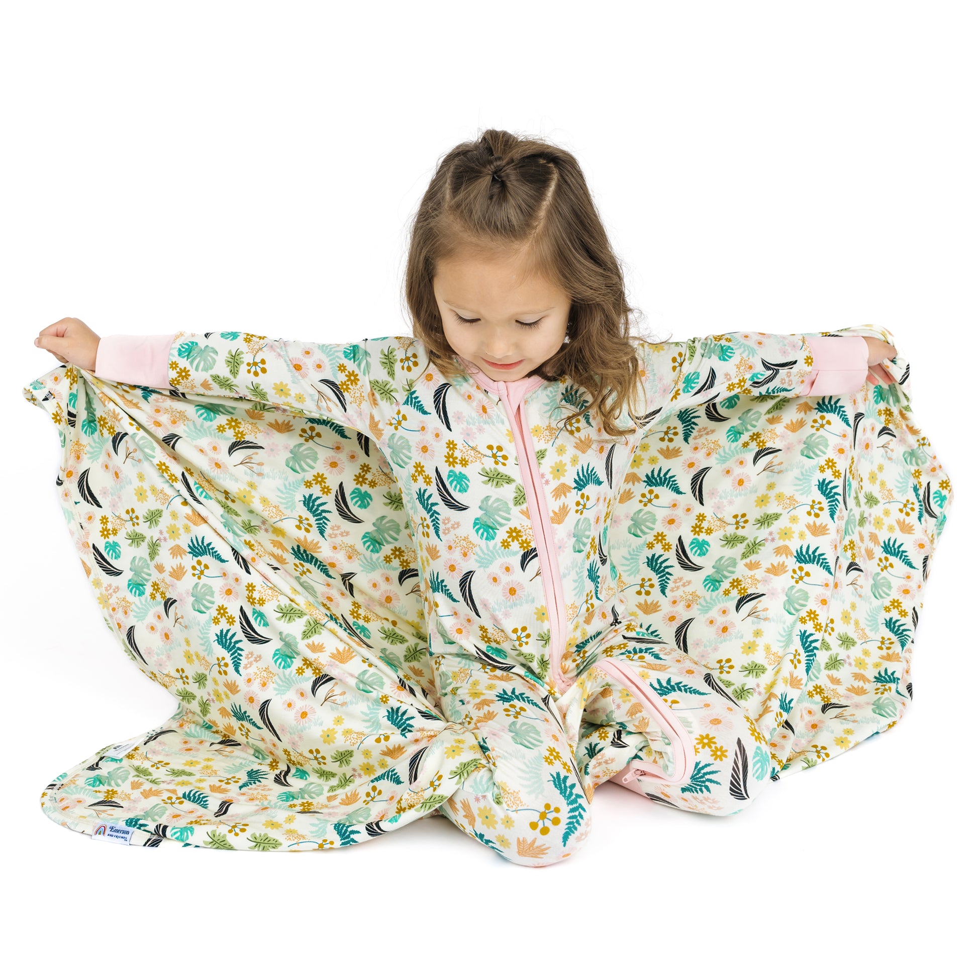 Toddler girl holding up the large Tropical Blooms bamboo blanket, highlighting the lightweight and breathable fabric.