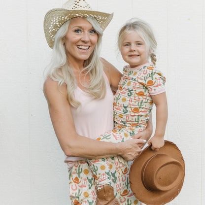 Woman and child in matching outfits with a straw hat against a white background