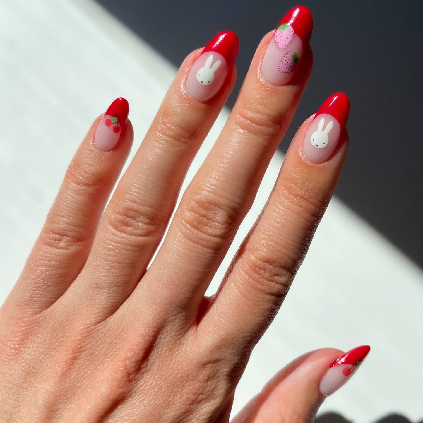 Close-up of a hand with red and white nail polish on a neutral background