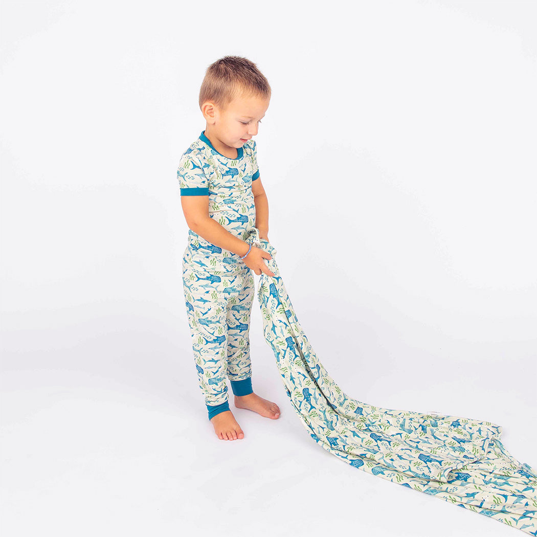 Little boy wearing our Shark Friends Two Piece Bamboo Pajama Set, holding up our Shark Friends Bamboo Blanket.