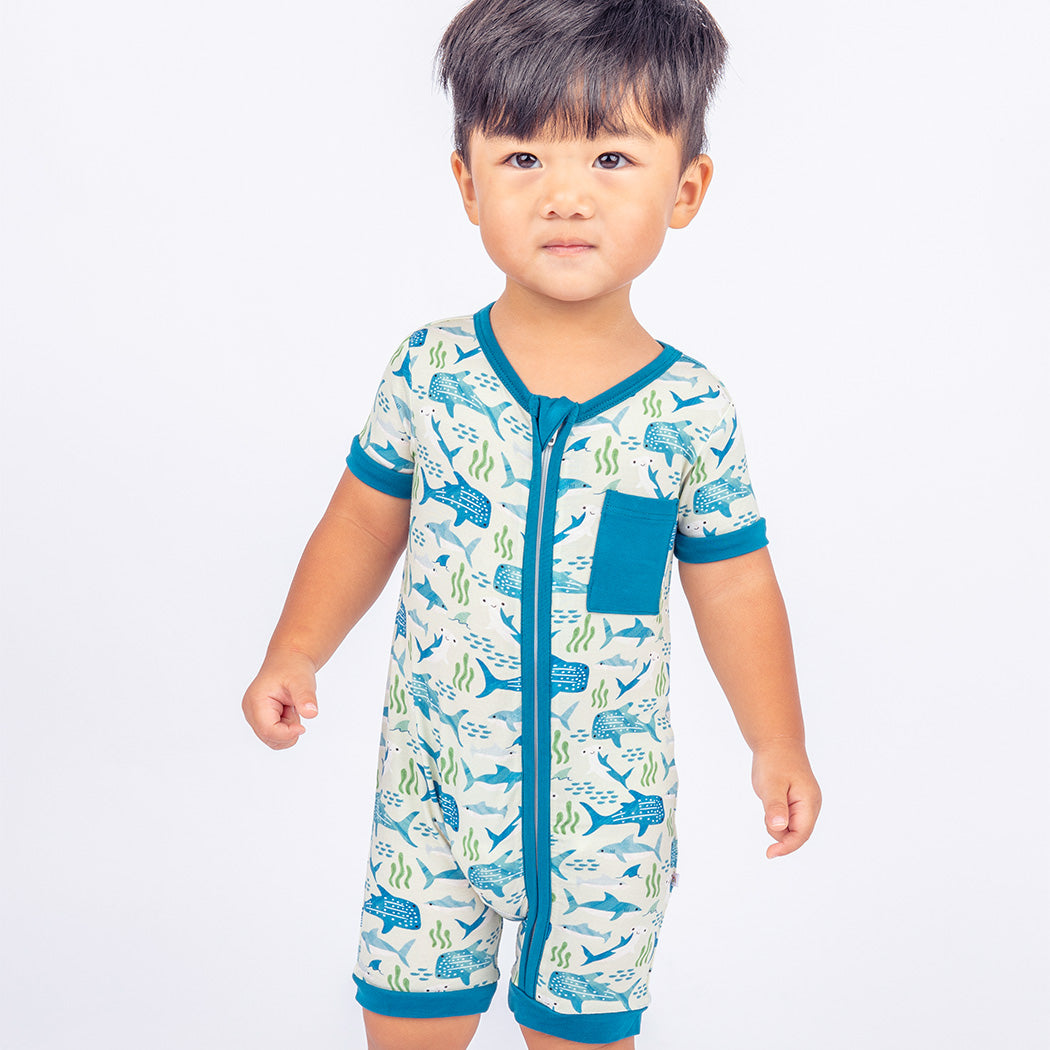 Little boy standing while wearing our Shark Friends Shortie Romper.