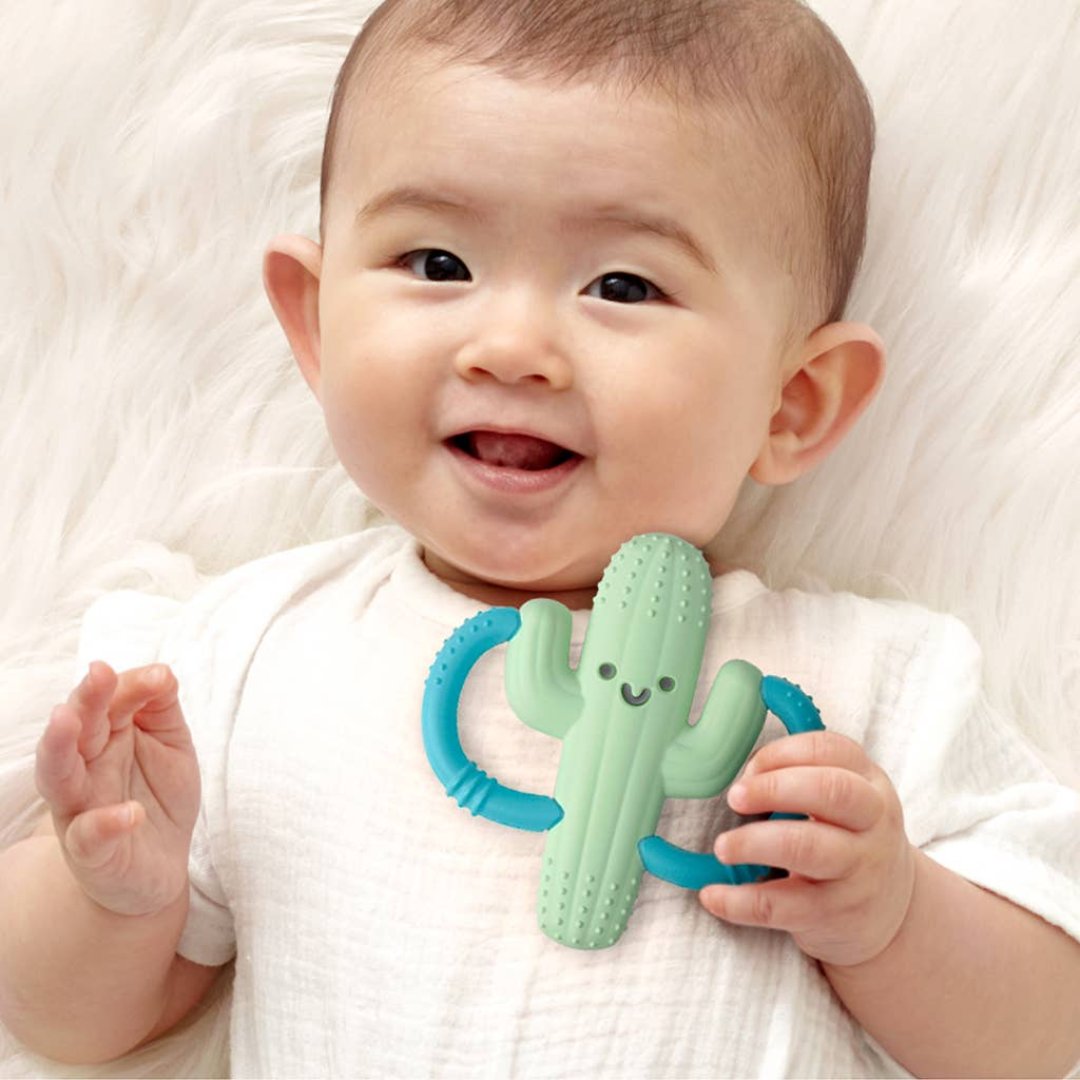 baby laying down holding onto a cactus shaped baby teether