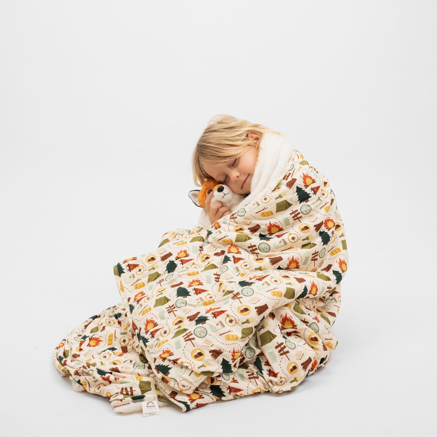 Child sitting wrapped in Camp Emerson bamboo and fleece throw blanket with camping print.