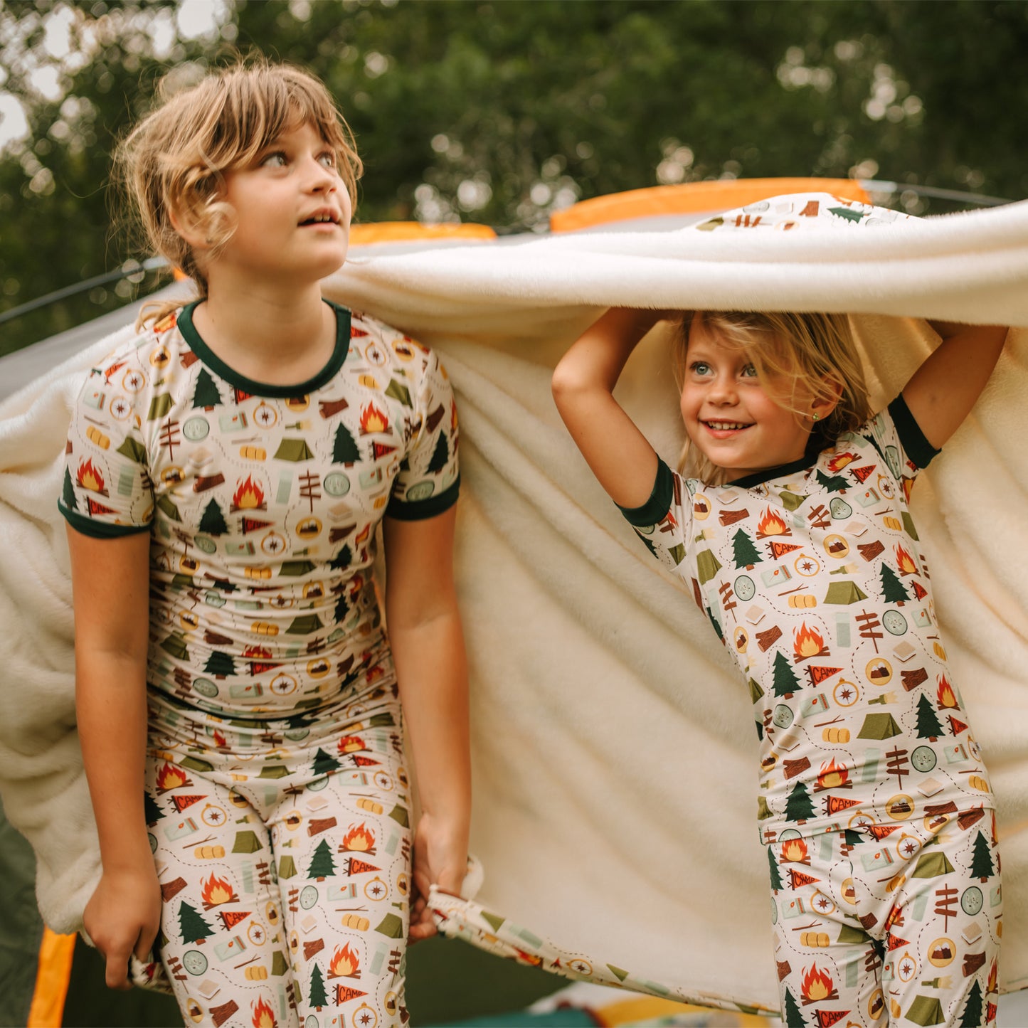 Siblings holding up Camp Emerson bamboo fleece throw blanket with camping print.