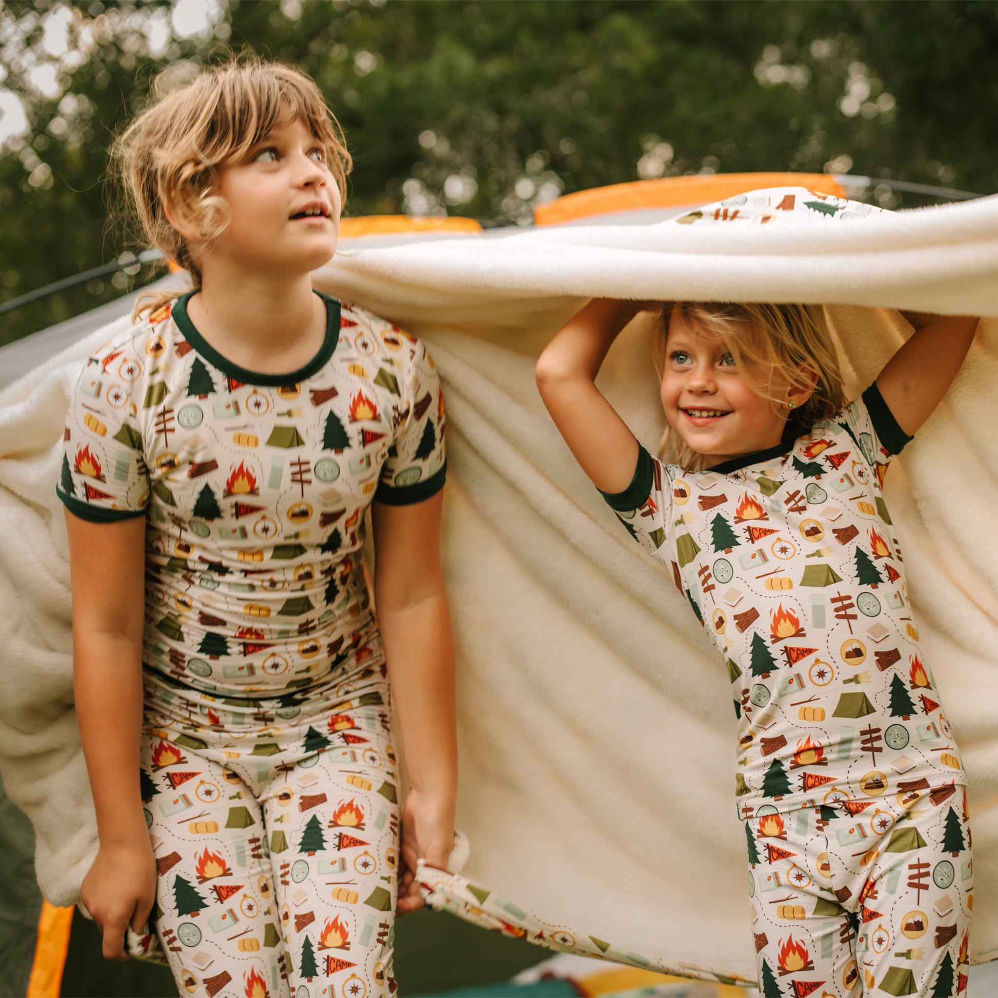 Siblings holding up Camp Emerson bamboo fleece throw blanket with camping print.