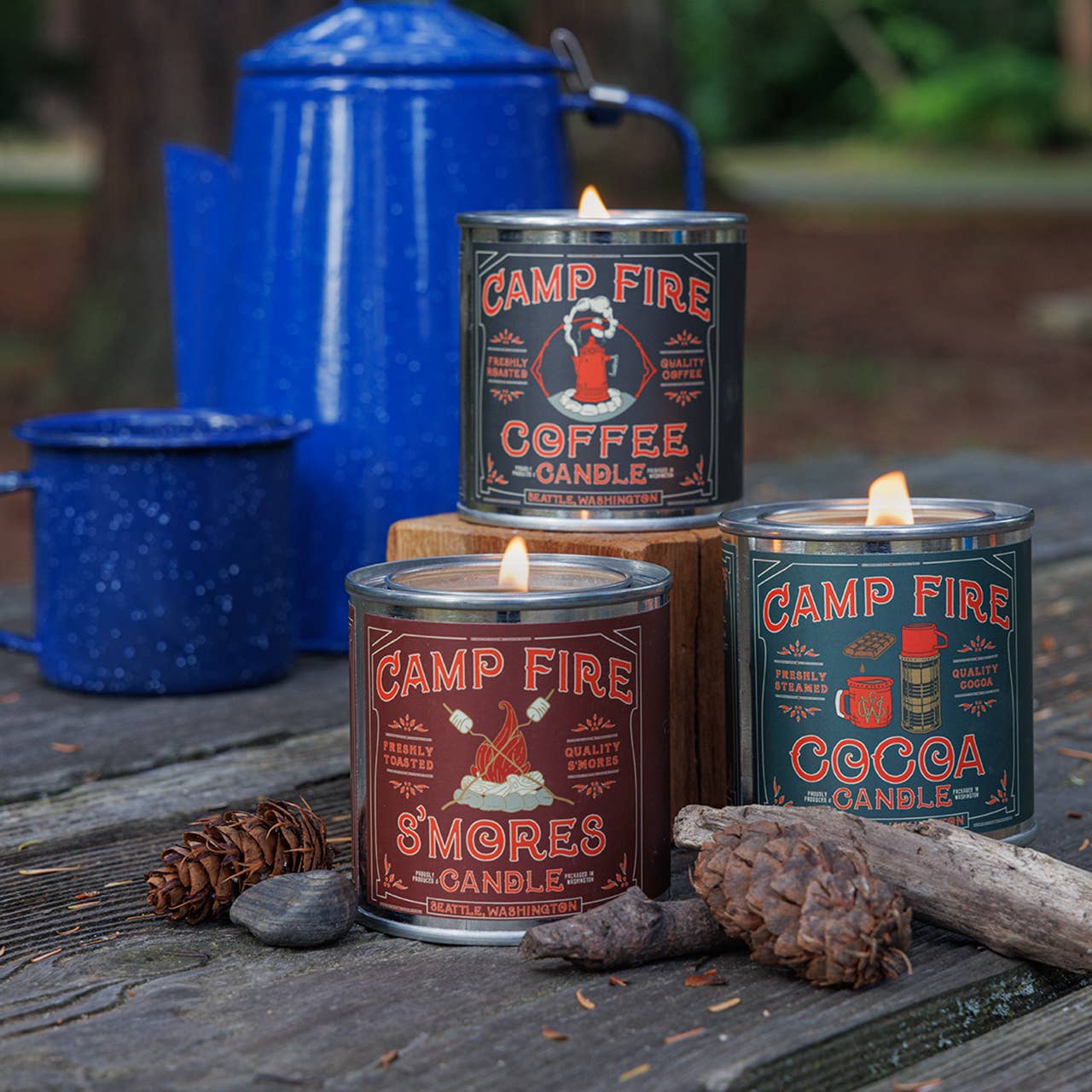 Campfire-themed candles with labels on a wooden surface with blue containers in the background.