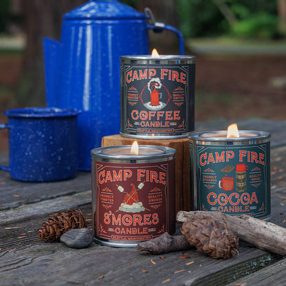 Campfire-themed candles with labels on a wooden surface with blue containers in the background.